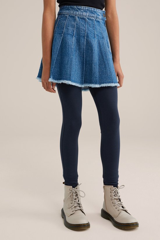 Meisje in donkerblauwe legging onder een spijkerrok, met witte laarzen.