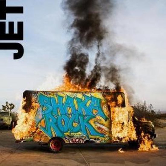 Een brandende bestelbus met de tekst "SHAKA ROCK" in graffiti, de letters zijn blauw met een gele omtrek.