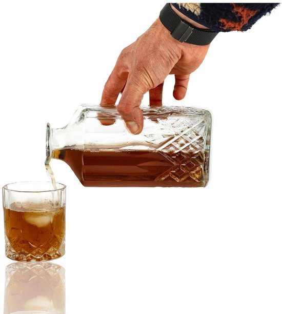 Hand schenkt amberkleurige drank uit een diamantpatroon karaf in een glas met ijs.