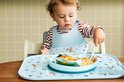 Een baby met een lichtblauw slab met vosjesprint eet uit een lichtblauw bord op een bijpassende placemat.