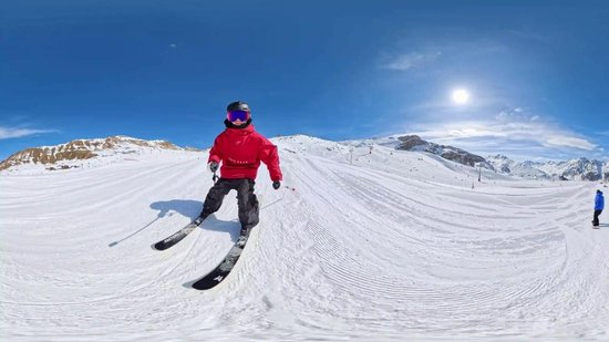 Skiër in rood jack skiet op besneeuwde piste met blauwe lucht.