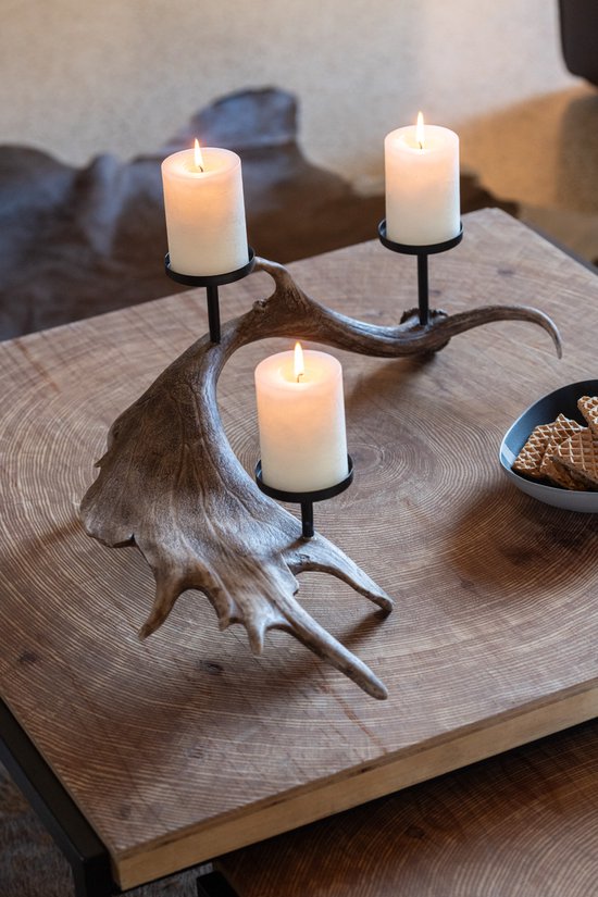 Een bruine hertengewei kandelaar met drie brandende witte kaarsen, geplaatst op een houten tafel.