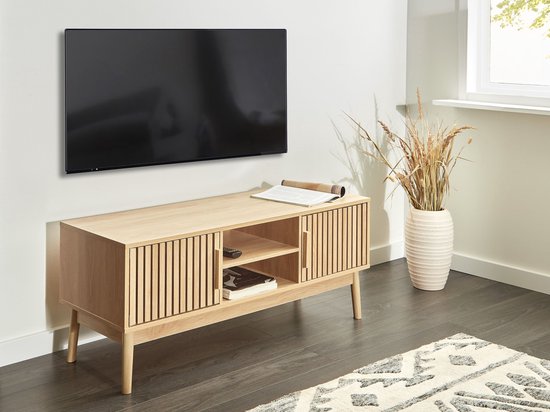 Licht houten tv-meubel met lamellen deuren, onder een tv in een woonkamer.