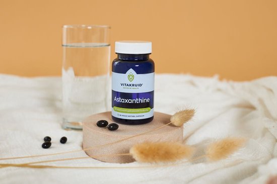 Paarse pot met Astaxanthine capsules, glas water en gedroogde planten.