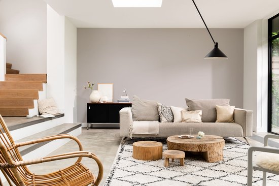 Een woonkamer met een lichte stoffen bank, houten tafels, een rotan stoel en een vloerkleed met grafische patronen.