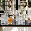 Verres à motif losange sur une table en marbre, dont un grand verre avec une boisson et une garniture.