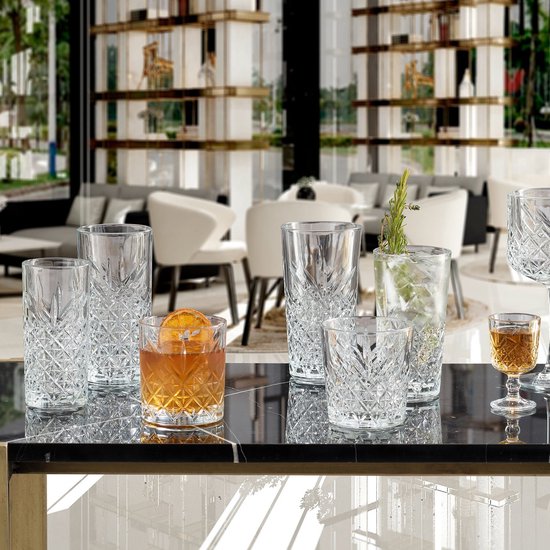 Verres à motif losange sur une table en marbre, dont un grand verre avec une boisson et une garniture.