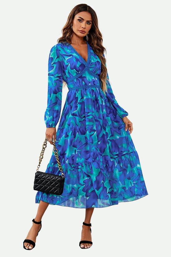 Maxi-jurk met lange mouwen, diepe V-hals en blauwe bloemenprint, gedragen door model met zwarte tas.