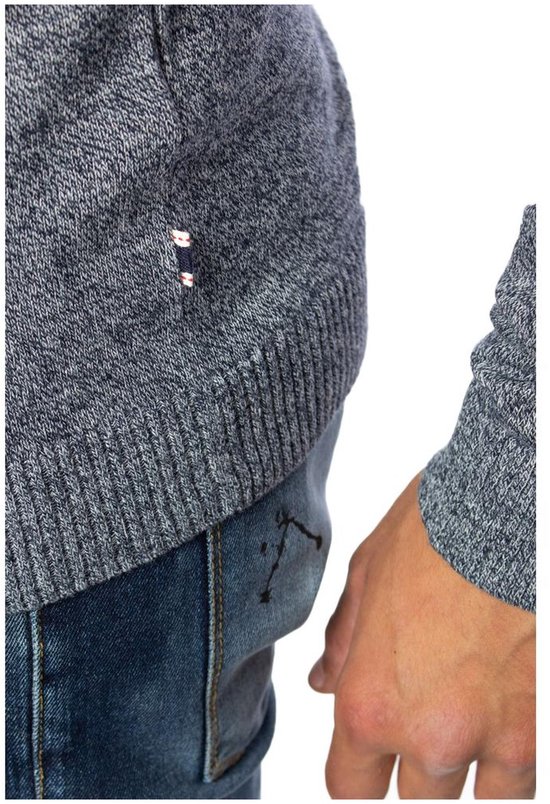 Gedetailleerd beeld van de onderkant van een grijze gebreide trui met een klein logo en een spijkerbroek.