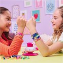 Twee meisjes met zelfgemaakte armbandjes in felgekleurde tinten, met de armbandjesmaker op tafel.