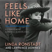Boekcover met 'FEELS LIKE HOME A SONG FOR THE SONORAN BORDERLANDS LINDA RONSTADT AND LAWRENCE DOWNES' in tekst. Een kind met sombrero kijkt weg.