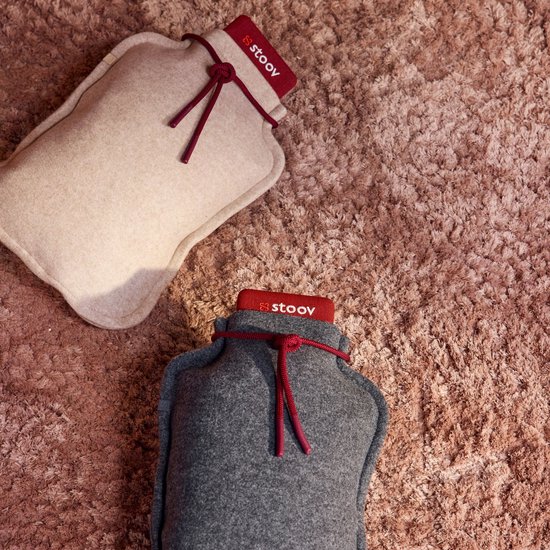 Twee Stoov infrarood warmtekruiken in beige en grijs met rood koord op een pluizige ondergrond.
