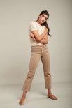 Model in crème gebreide top met korte mouwen en beige jeans. Ze draagt puntige instappers.