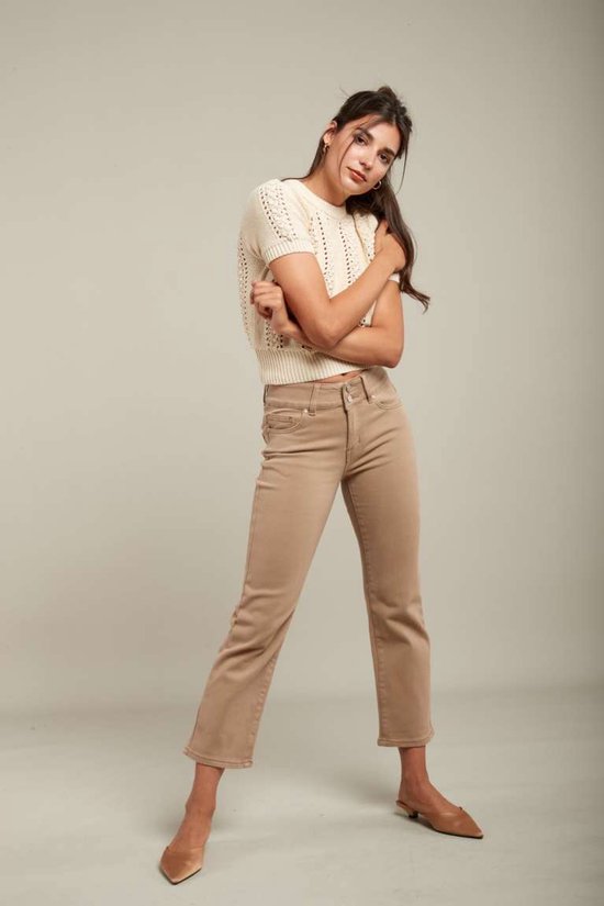 Model in crème gebreide top met korte mouwen en beige jeans. Ze draagt puntige instappers.