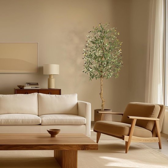 Kunstmatige olijfboom met groene bladeren en olijven, in een woonkamer met een witte bank en bruin fauteuil.
