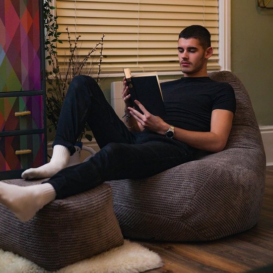 Man leest een boek in een lila beanbag stoel, met zijn voeten op een bijpassende poef. Zittend op een houten vloer.