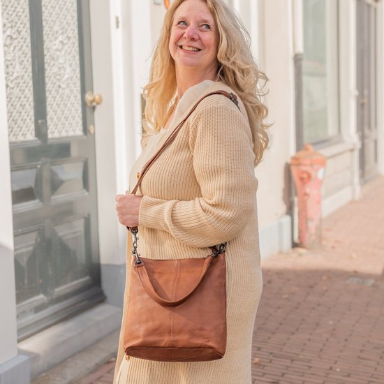 Vrouw met een blonde krullenbol en een lange beige cardigan, draagt een bruine leren schoudertas.