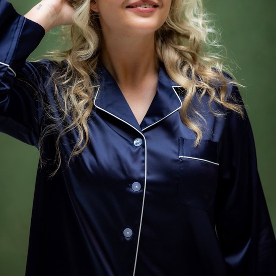 Close-up van model met blond haar, draagt een donkerblauwe satijnen pyjamajas met witte biesjes en knoopjes.