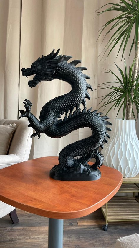 Zwart drakenornament op een tafel, met gordijnen en planten op de achtergrond.