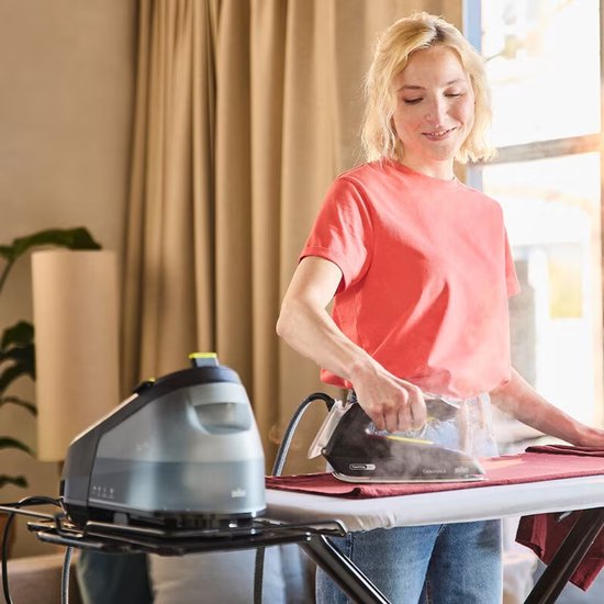 Vrouw met rood shirt en spijkerbroek, strijkt met een zwart Braun CareStyle 3 strijkijzer over een rood textiel. Zwarte stoomgenerator ernaast.