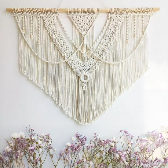 Crèmekleurig macramé wandkleed met franjes, houten stok, kralen, bij bloemen.