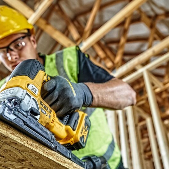 Een bouwmedewerker snijdt een plank met een DeWalt decoupeerzaag.