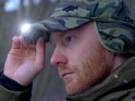 Man met rode baard die een camouflage pet met verlichte klep opzet.
