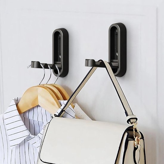 Twee zwarte, opklapbare wandhaken aan een witte muur met kleding en een tas.