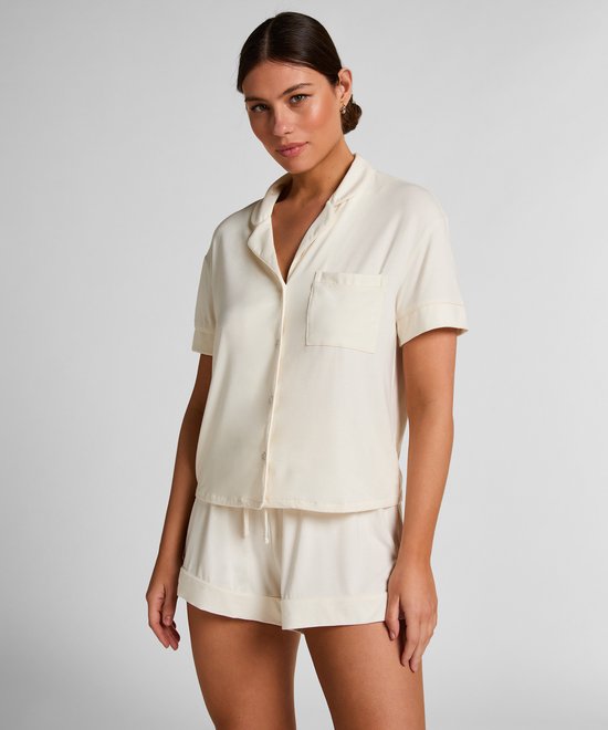 Model in gebroken witte pyjamashirt en short, staand met een hand in haar broekzak.