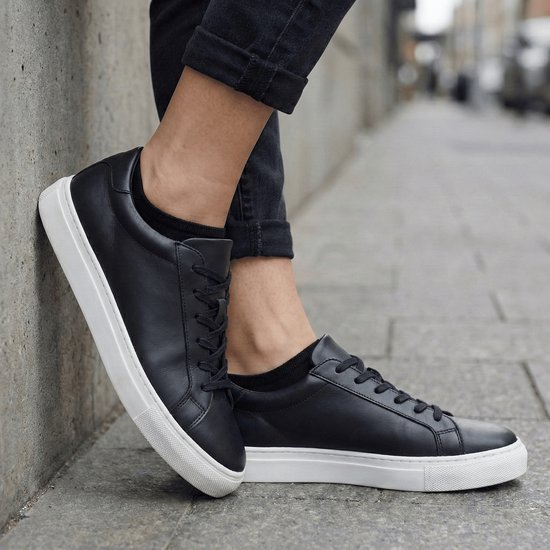 Een persoon draagt zwarte sneakersokken met zwarte leren sneakers.