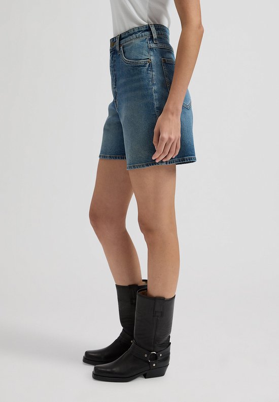 Zijaanzicht van een vrouw in een spijkerbroek met wijde pijpen, die zwarte cowboylaarzen draagt.