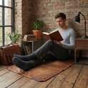 Man leest een boek op de houten vloer. Hij draagt een grijs shirt en een grijze broek, met Sukats antraciet sokken met rode streep.