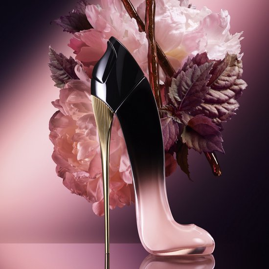Roze en zwarte pump-vormige parfumfles met gouden hak, met roze bloemen en bladeren op de achtergrond.