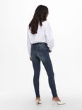 Model in een witte blouse en donkerblauwe skinny jeans, gezien van achteren. Witte blouse met wijde mouwen en witte puntige muiltjes.