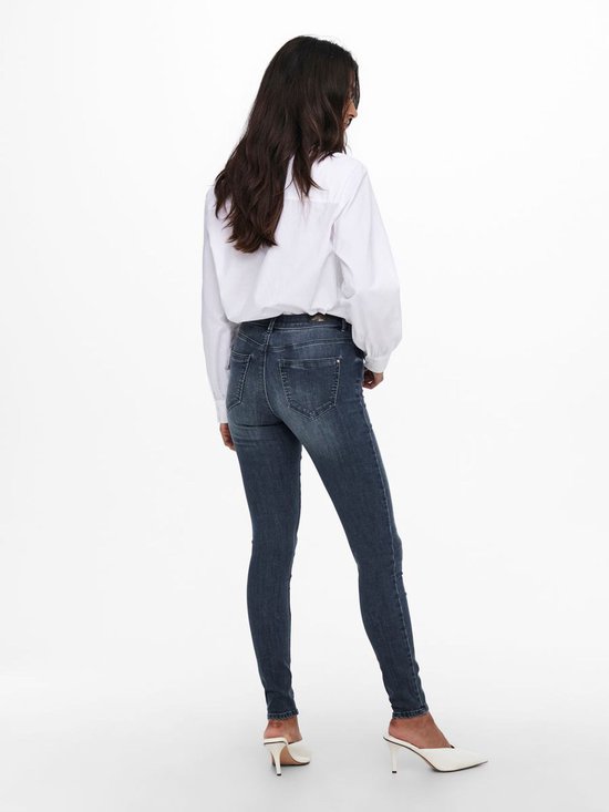 Model in een witte blouse en donkerblauwe skinny jeans, gezien van achteren. Witte blouse met wijde mouwen en witte puntige muiltjes.