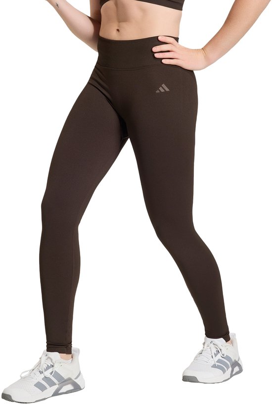 Gedetailleerde kijk op de benen van een vrouw in een bruine legging, met een sportbeha en witte sportschoenen.