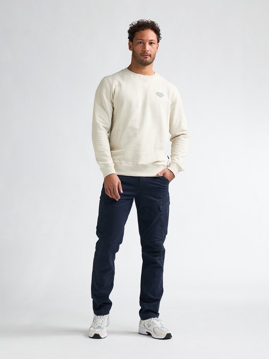 Man draagt een beige sweater en donkerblauwe cargobroek met opgestikte zakken.