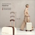 Femme avec un carré blond dans une tenue beige tenant une valise blanc cassé à roulettes avec une poignée télescopique.