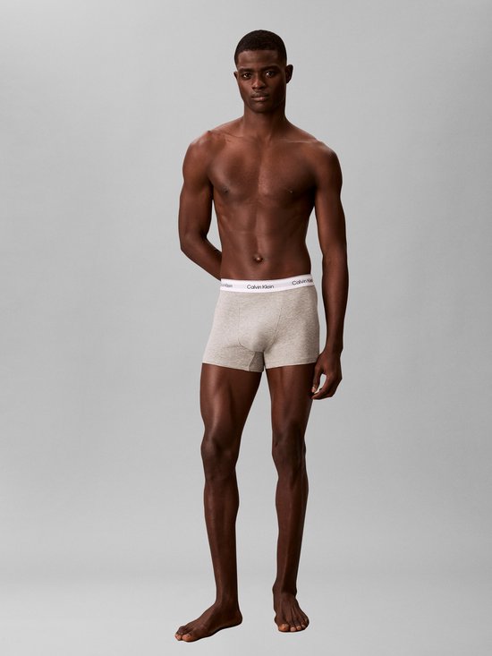 Man met getinte huid draagt lichtgrijze Calvin Klein boxershorts, handen achter rug, staand.