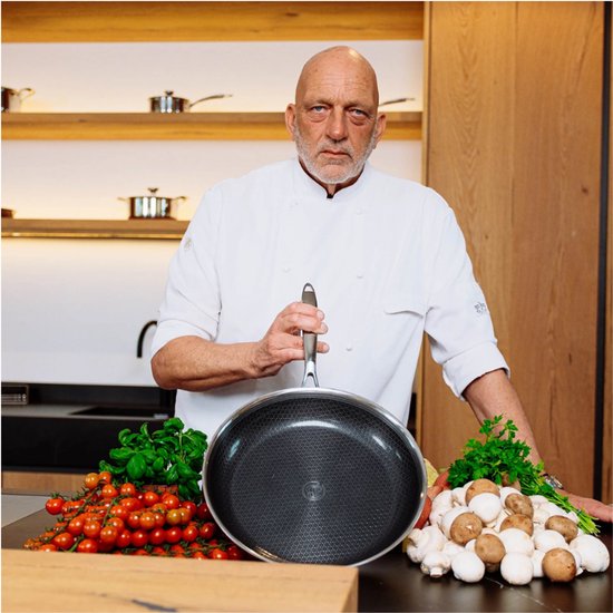Chefkok met pan in keuken, omringd door groenten.