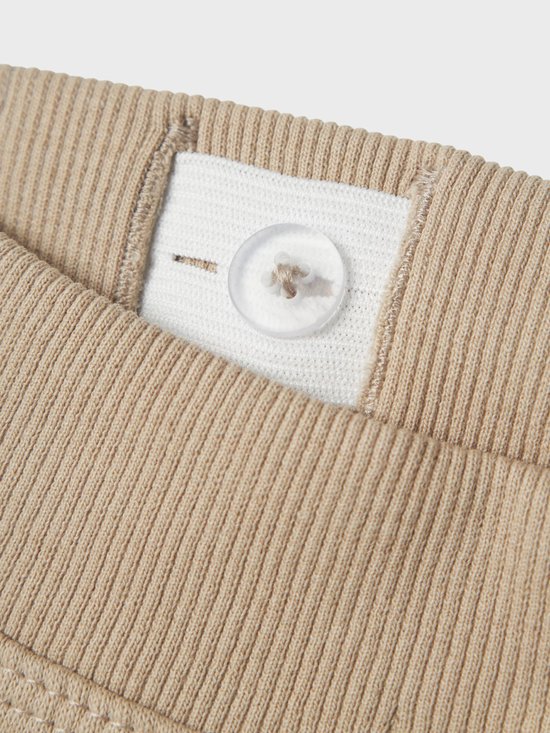 Detail van de tailleband van een beige joggingbroek met knoopsluiting.