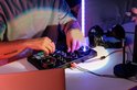 Dichtbij een DJ-controller waarop een persoon de knoppen bedient, met een laptop, koptelefoon en rode smartphone.