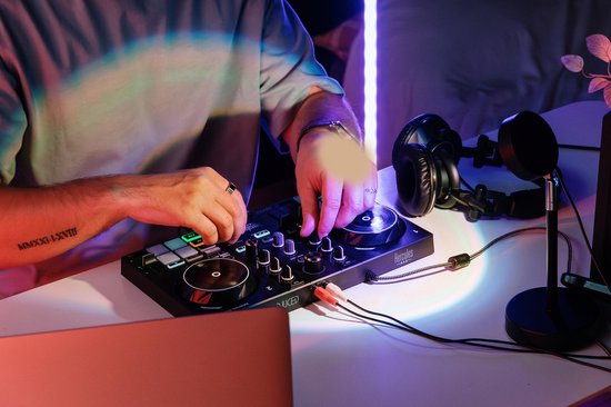 Dichtbij een DJ-controller waarop een persoon de knoppen bedient, met een laptop, koptelefoon en rode smartphone.