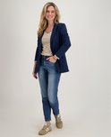 Vrouw met blonde krullen, draagt een donkerblauwe blazer over een gestreepte top en blauwe jeans.