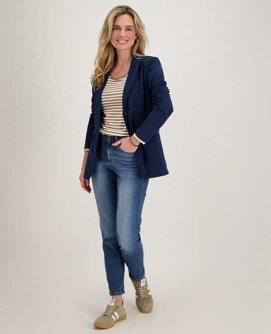 Vrouw met blonde krullen, draagt een donkerblauwe blazer over een gestreepte top en blauwe jeans.
