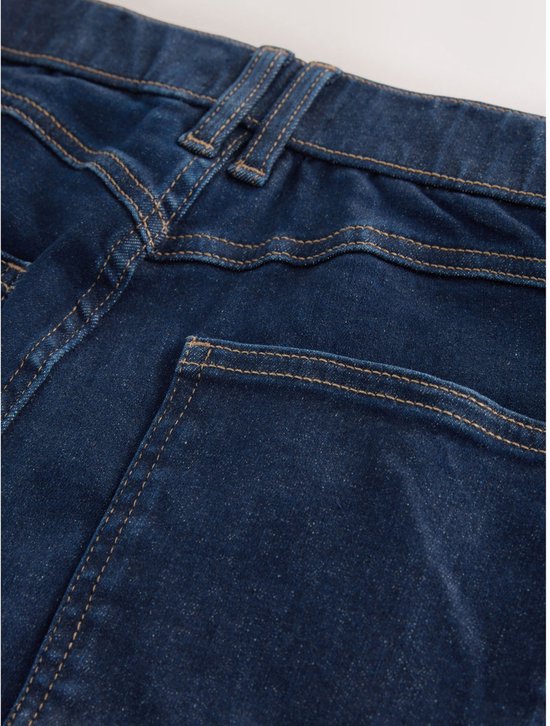 Sluiting en zakdetails van een donkerblauwe spijkerbroek met zichtbare oranje stiksels.