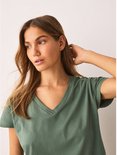 Close-up van een vrouw met lang blond haar, dragend een groen V-hals T-shirt.