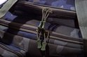 Detail van dubbele ritsen met groene touwtjes aan de camouflage tas.