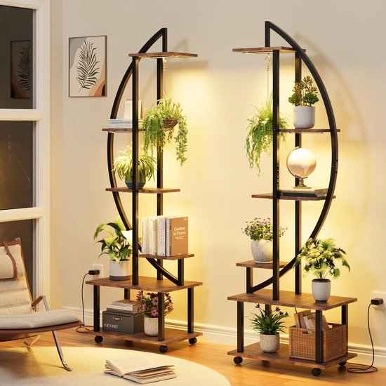 Twee 6-laags plantenrekken met planten, boeken en decoraties, verlicht door groeilampen, in een woonkamer.