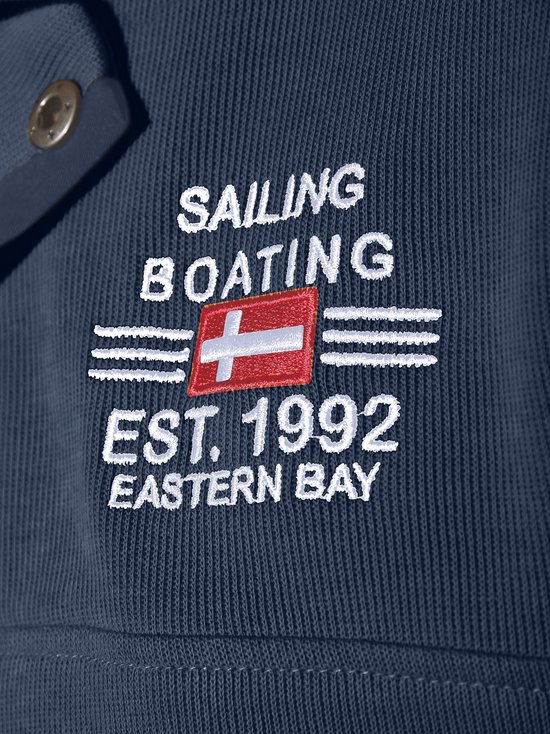 Detailopname van de opdruk 'SAILING BOATING EST. 1992 EASTERN BAY' op een donkerblauwe ribgebreide trui.